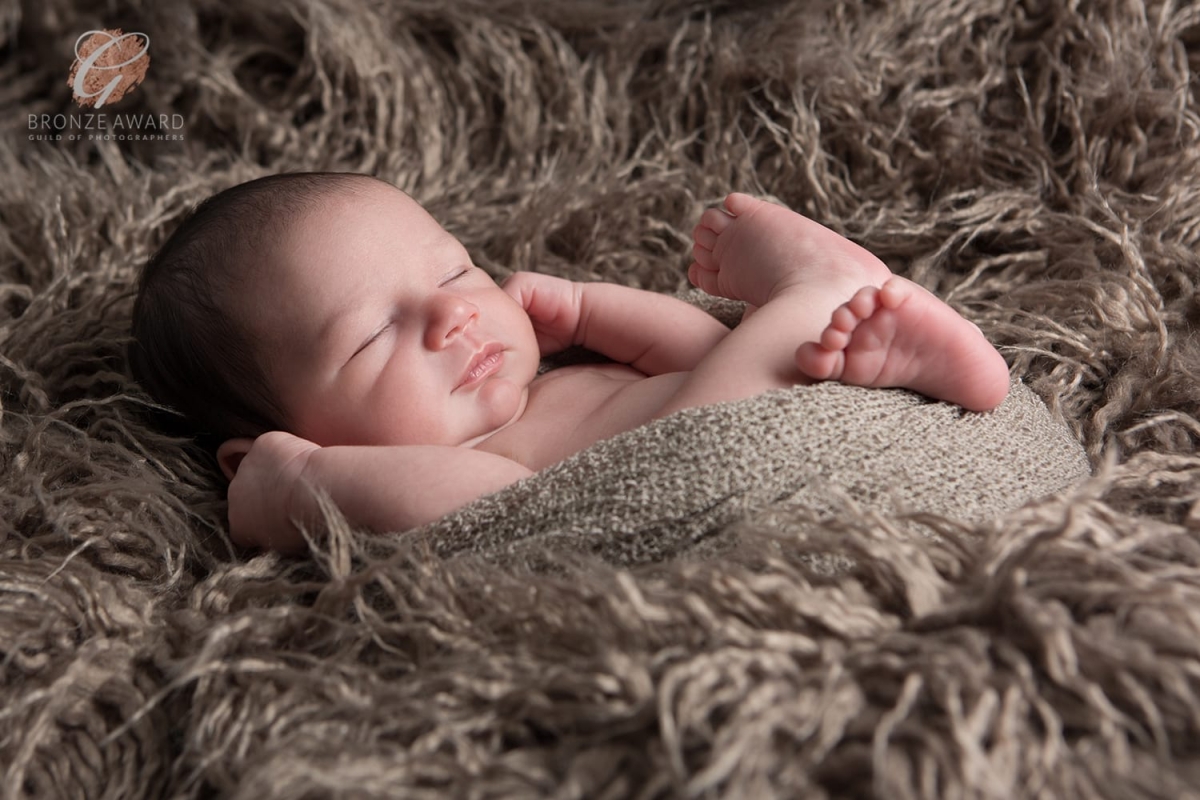 Bronze award for newborn curled up on a flokati blanket with his arms up