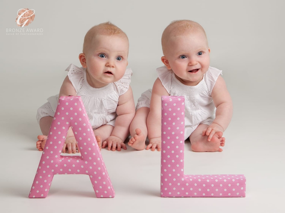 Bronze award for beautiful twin girls sitting behind large pink letters