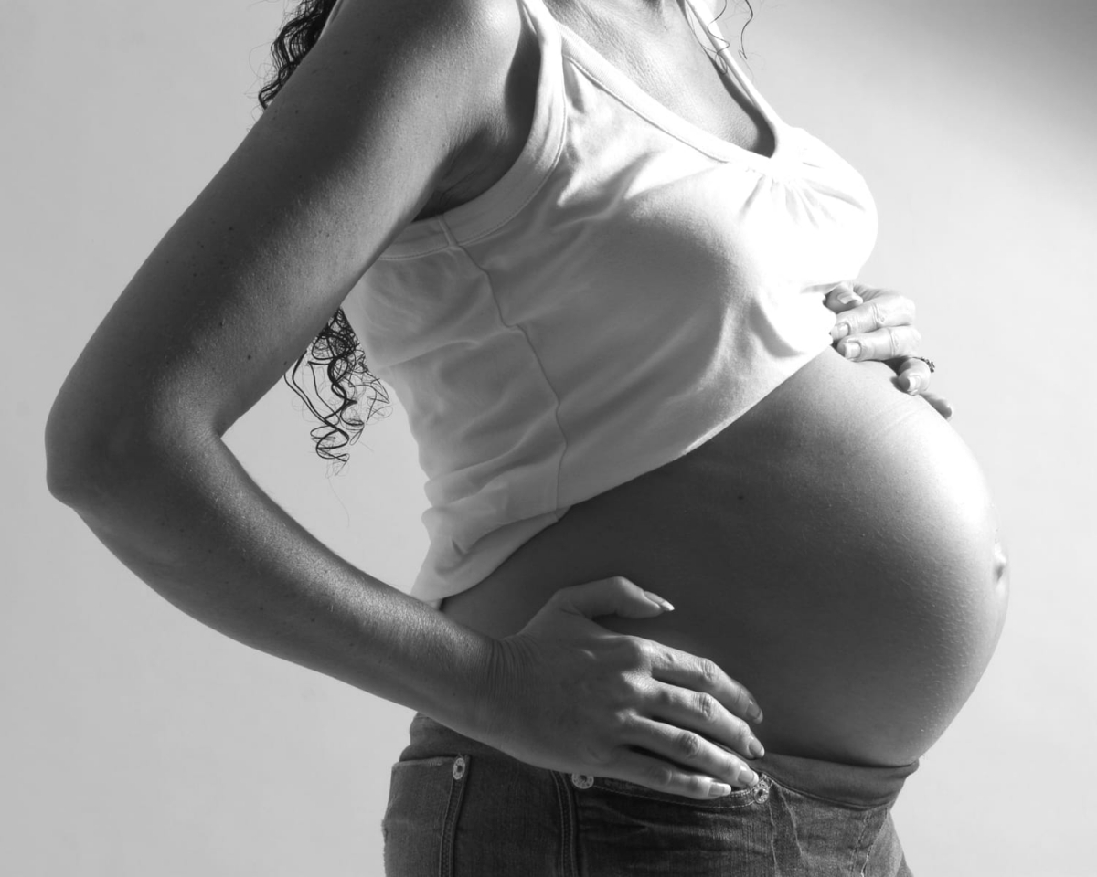 Side shot of pregnant women wearing a white thin strap top pushed up over bump