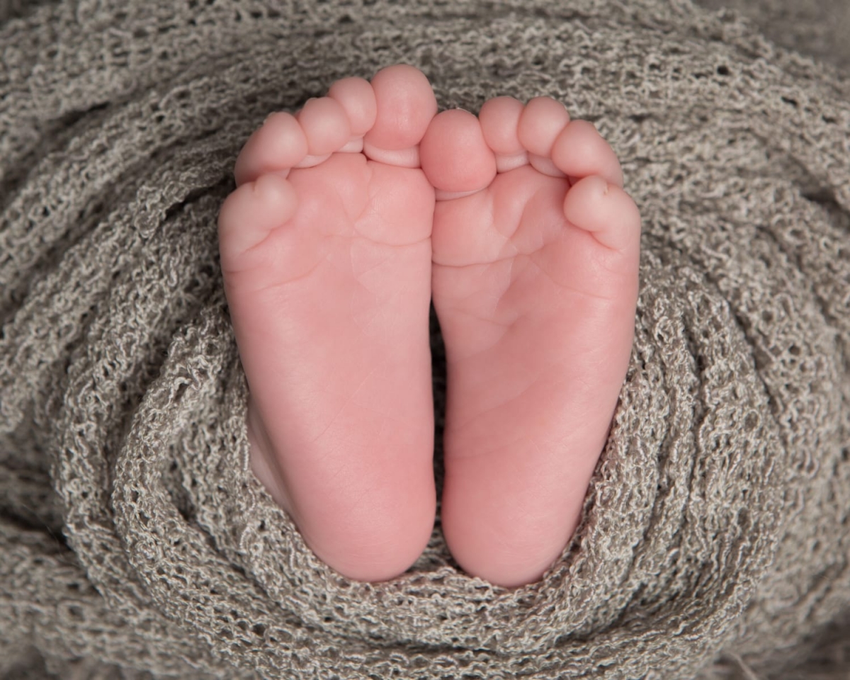 Close up photograph of newborn baby feet with a grey wrap